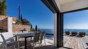 Una terraza de madera con una mesa y sillas, con vista a un cielo azul despejado y una masa de agua.