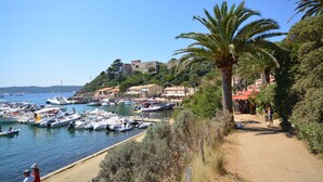 Una marina costera con barcos amarrados, un sendero de arena y edificios al fondo.