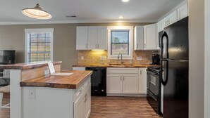 Una cocina moderna con armarios blancos, un refrigerador negro, un lavavajillas y una encimera de madera.