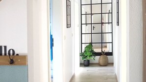 A hallway with wooden beams, a black grid door, and a potted plant. - 6P wooden house + garden on the Elbe dike | modern, close to nature, family & dog-friendly (Artlenburg)