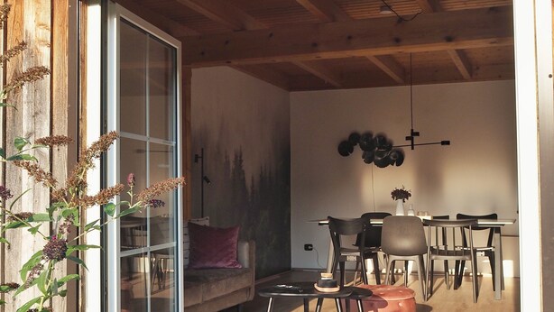 A modern interior with a dining area, a sofa, and a staircase leading to a second floor. - 6P wooden house + garden on the Elbe dike | modern, close to nature, family & dog-friendly (Artlenburg)