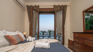 Ein Hotelzimmer mit Bett, einem hölzernen Schminktisch und Blick auf Pool und Palmen durch die offenen Vorhänge.