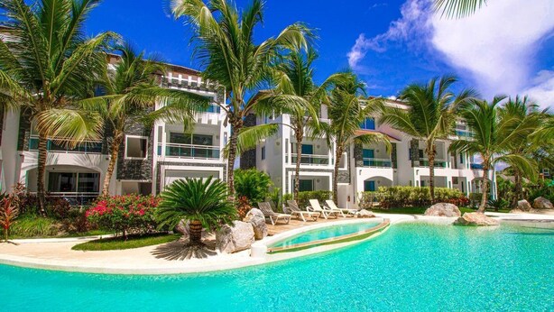 Un resort con una piscina circondata da palme e un edificio a più piani con balconi.