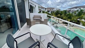 Un balcone con una porta in vetro, un tavolo rotondo, due sedie e vista su una piscina e altri edifici.