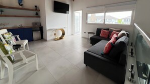 Un ampio soggiorno dal design moderno, con un divano nero, una poltrona bianca, una TV a parete e un soffitto in legno.