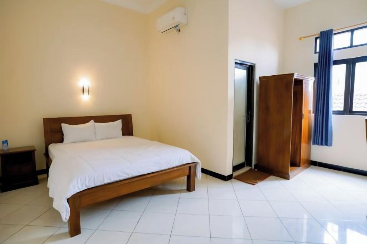 Una habitación de hotel con cama, mesita de noche, armario y ventana con cortinas.