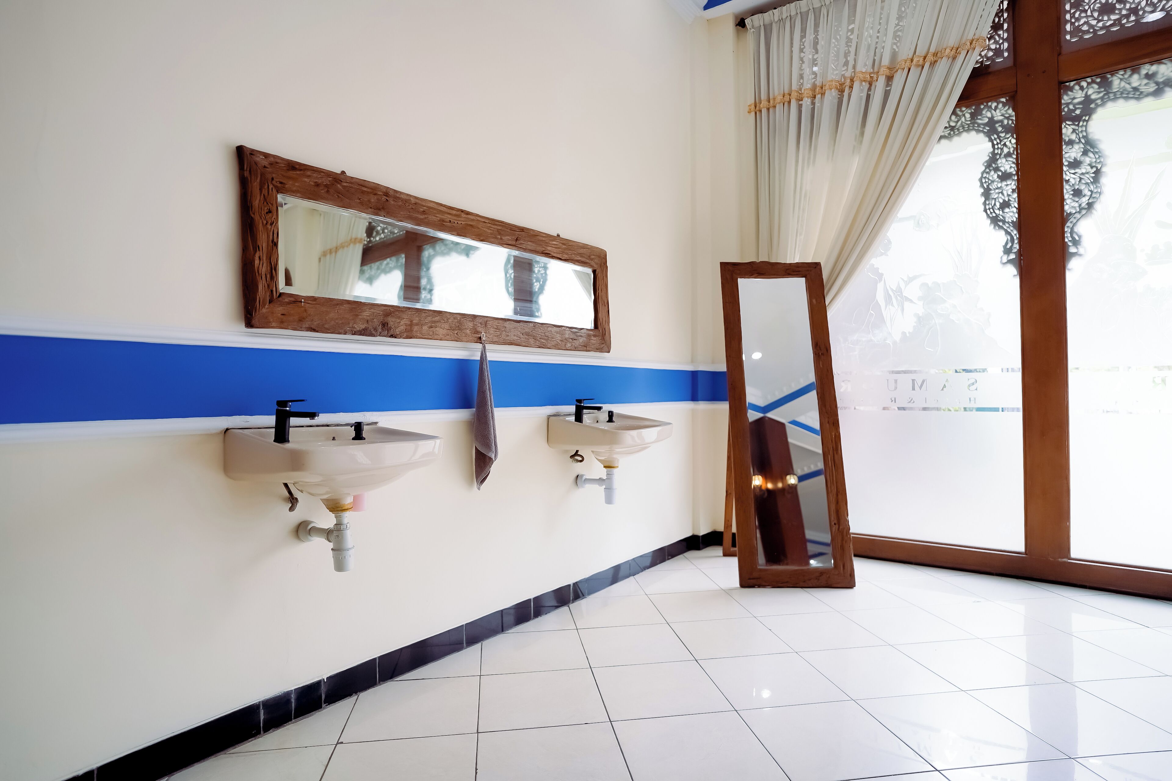 Un baño con dos lavamanos, un espejo y una ventana con cortinas.