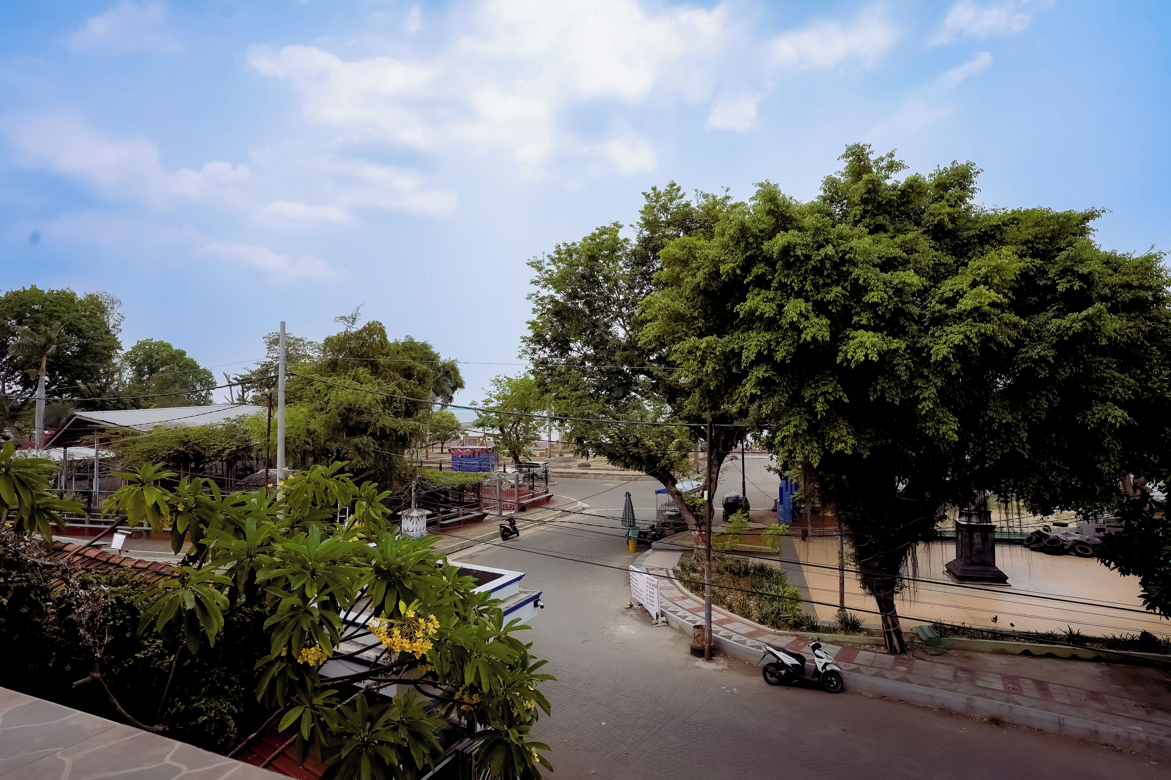 A street view with a tree-lined road, a parked scooter, and a blue boat in the foreground.