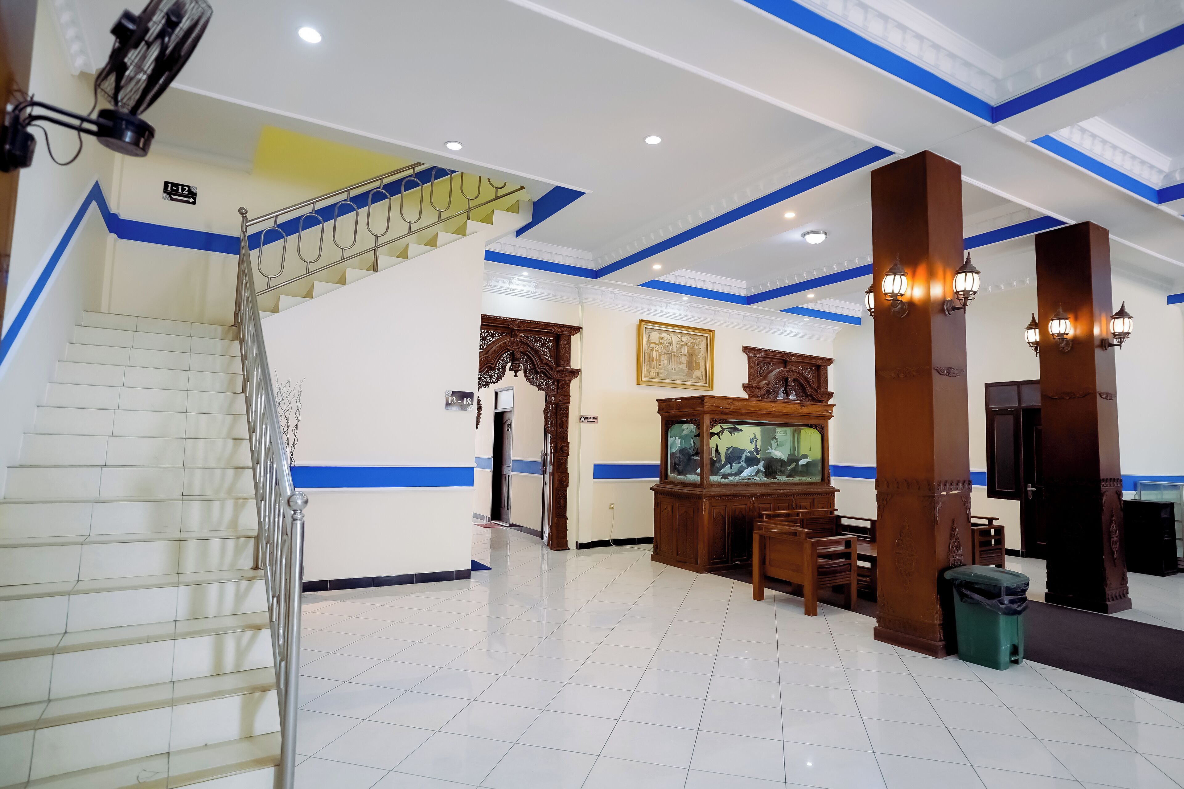 A hotel lobby with a staircase, a reception desk, a fish tank, and a dining area.