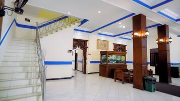 A hotel lobby with a staircase, a reception desk, a fish tank, and a dining area.
