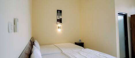 A hotel room with a bed, a nightstand, a wall-mounted light, and a door.