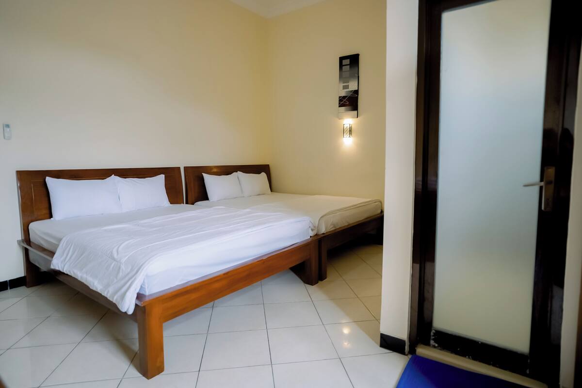 Quarto de hotel com uma cama de madeira, uma cama menor e um aplique na parede.