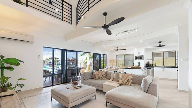 A spacious living area with a sofa, ottoman, and a dining table. There is a balcony with a view of the city. - Villa Utopia on the Marina | 3 Bed, 3 Bath by Tropical BNB (Stuart Park)