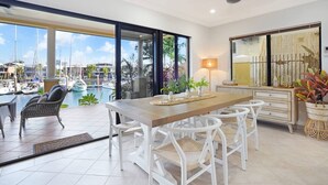 A spacious dining area with a view of a marina, a wooden table, white chairs, and a modern lamp. - Villa Utopia on the Marina | 3 Bed, 3 Bath by Tropical BNB (Stuart Park)