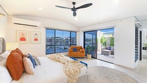 A modern bedroom with a large bed, a ceiling fan, and a view of a marina through large windows. - Villa Utopia on the Marina | 3 Bed, 3 Bath by Tropical BNB (Stuart Park)