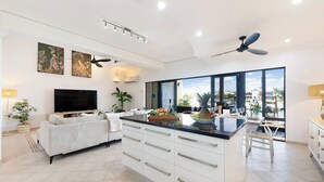 A modern kitchen with a central island, large windows offering a view of the sea, and a dining area with a view. - Villa Utopia on the Marina | 3 Bed, 3 Bath by Tropical BNB (Stuart Park)