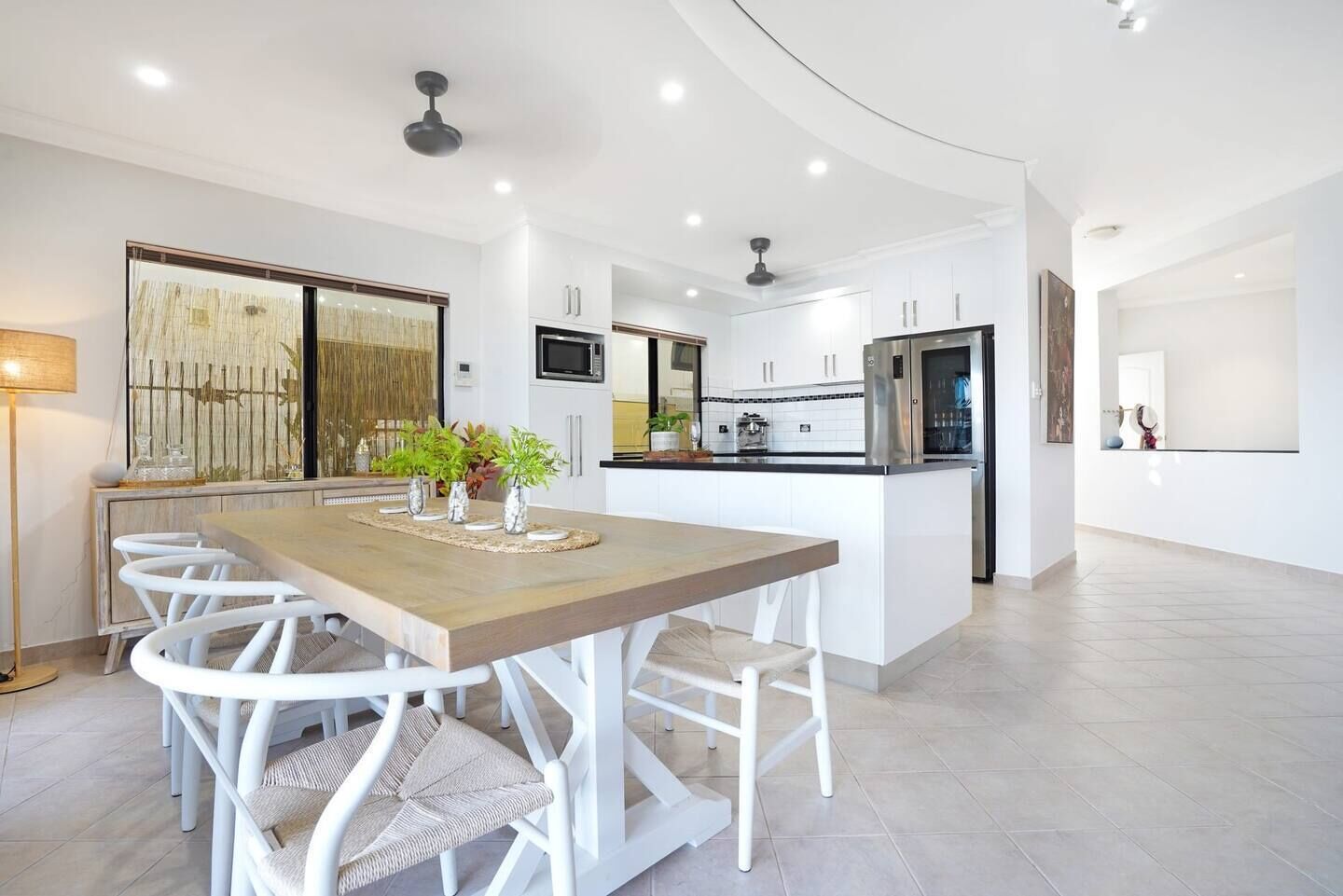 A modern kitchen with white cabinetry, a central island, and a dining area with white chairs.