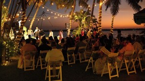 A beachside event with chairs arranged in rows facing a stage, palm trees, and string lights. - Village Canopy | wedding venues kochi (Kochi)