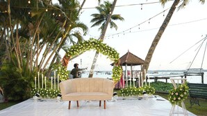 An outdoor stage with a sofa, surrounded by palm trees and a decorative arch. - Village Canopy | wedding venues kochi (Kochi)