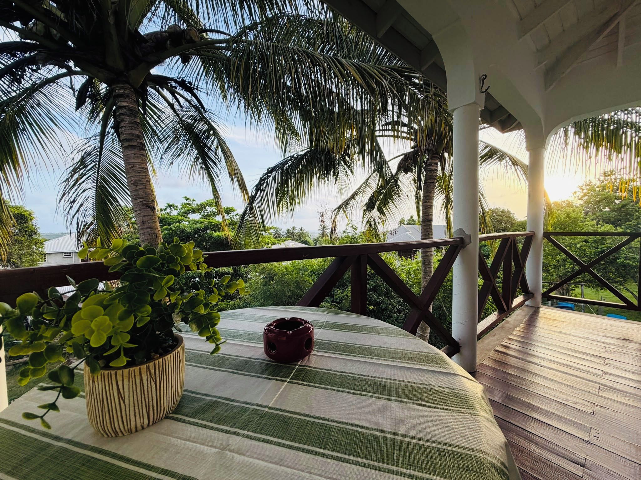 A covered outdoor area with a wooden deck, a table with a striped tablecloth, a potted plant, and a decorative item.