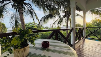 A covered outdoor area with a wooden deck, a table with a striped tablecloth, a potted plant, and a decorative item.