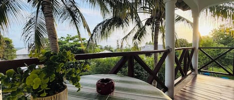 A covered outdoor area with a wooden deck, a table with a striped tablecloth, a potted plant, and a decorative item.