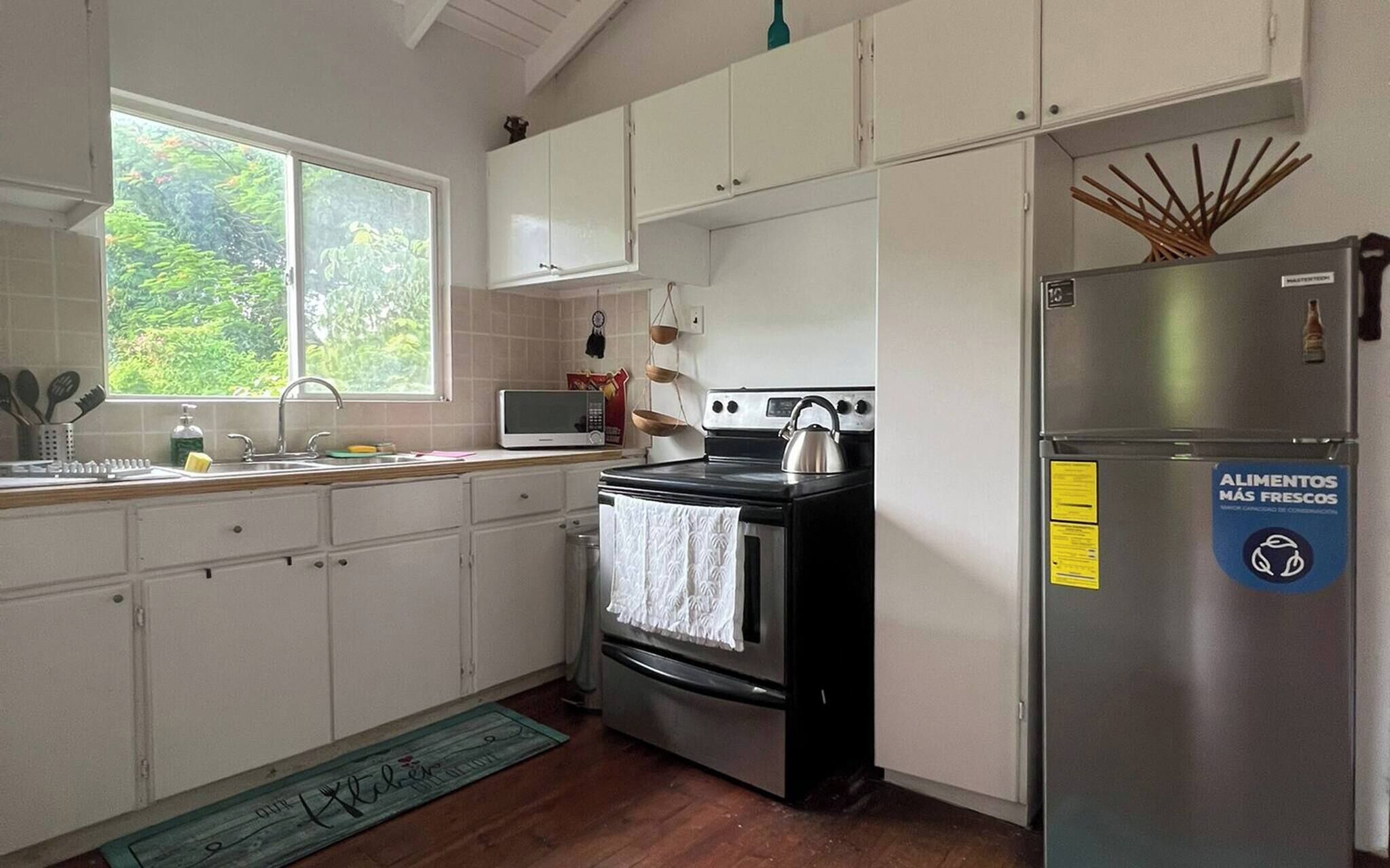 A kitchen with white cabinets, a stainless steel refrigerator, a stove, and a window with a view of greenery.