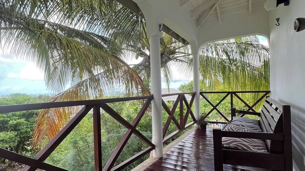 A covered outdoor seating area with a bench, surrounded by palm trees and a view of the landscape. - The Tree House - by Zenbreak (Workmans)