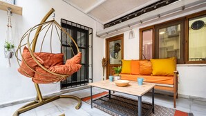 Un espacio de sala acogedor con una silla colgante, un sofá con cojines naranja, una mesa de centro de madera y una alfombra estampada.