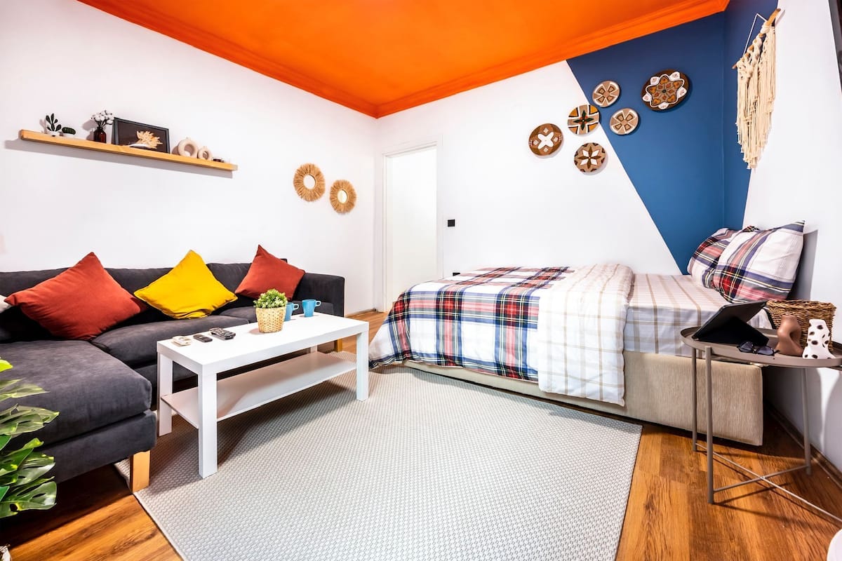 A modern living room with a sofa, coffee table, and a bed with a plaid bedspread.