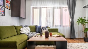 Una sala de estar moderna con un sofá verde, una mesa de centro de madera y un ventanal con cortinas translúcidas.