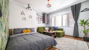 Un dormitorio moderno con una cama grande, un sofá verde, una mesita pequeña y una planta en maceta.