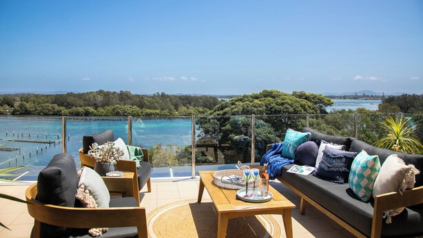 A terrace with a sofa, chairs, and a table, overlooking a body of water and greenery. - Regatta 19 - Top Floor Luxury.  Spectacular Water Views | Breathtaking Sunsets  (Forster)