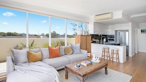 A modern living room with a sofa, coffee table, and a view of the kitchen. - Regatta 19 - Top Floor Luxury.  Spectacular Water Views | Breathtaking Sunsets  (Forster)
