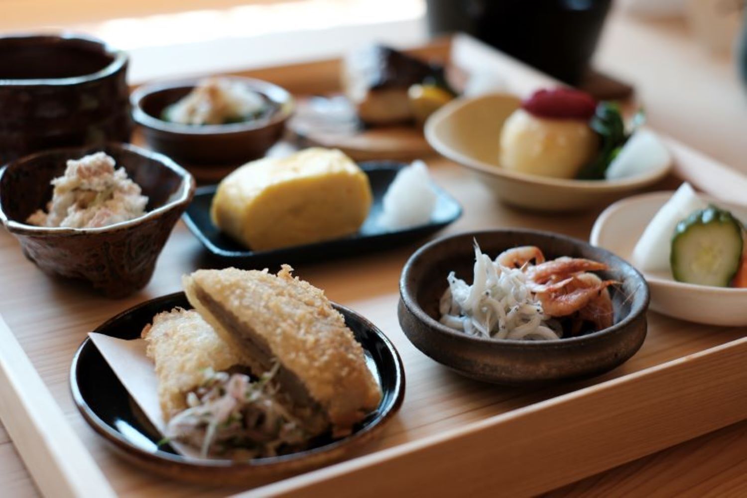 A variety of dishes on a wooden table, including a bowl of shredded vegetables, a plate with a breaded item, and a small dish with shrimp.