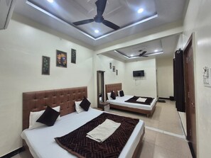 A hotel room with two beds, a ceiling fan, recessed lighting, a flat-screen TV, and a door with a handle. - Hotel Shiv Aagya (Ujjain)
