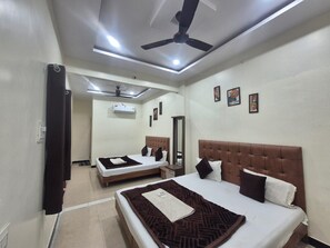A hotel room with two beds, a ceiling fan, and a mirror. - Hotel Shiv Aagya (Ujjain)