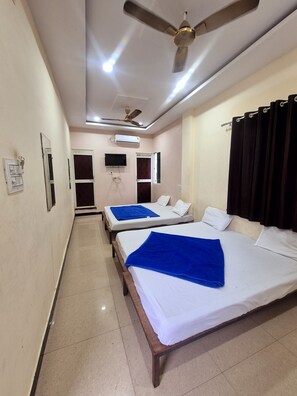 A hotel room with two beds, a ceiling fan, an air conditioning unit, and a television on the wall. - Hotel Shiv Aagya (Ujjain)