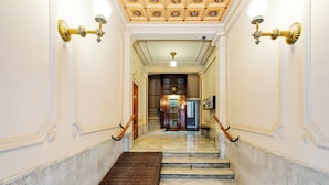 Una imponente escalera de mármol con barandilla de madera que conduce a una habitación con candelabro y puerta de madera.