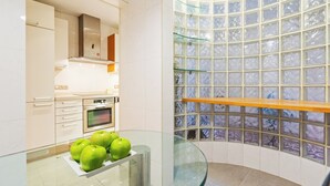 Una cocina moderna con una mesa de vidrio que muestra manzanas verdes, horno empotrado y una pared original de bloques de vidrio.