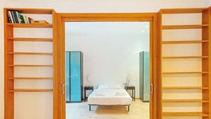Un dormitorio con cama, mesitas de noche, armario y estanterías abiertas.