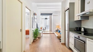 Een moderne keuken met roestvrijstalen apparatuur, een eethoek met tafel en stoelen, en een gang die leidt naar een slaapkamer.