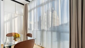 Een moderne kamer met een glazen tafel, twee stoelen, een fruitschaal en dunne gordijnen.