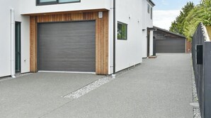 A modern two-story residential building with a large garage door, a wooden front porch, and a clear driveway. - Brand-new, townhouse - walking distance to Westfield Mall (Christchurch)