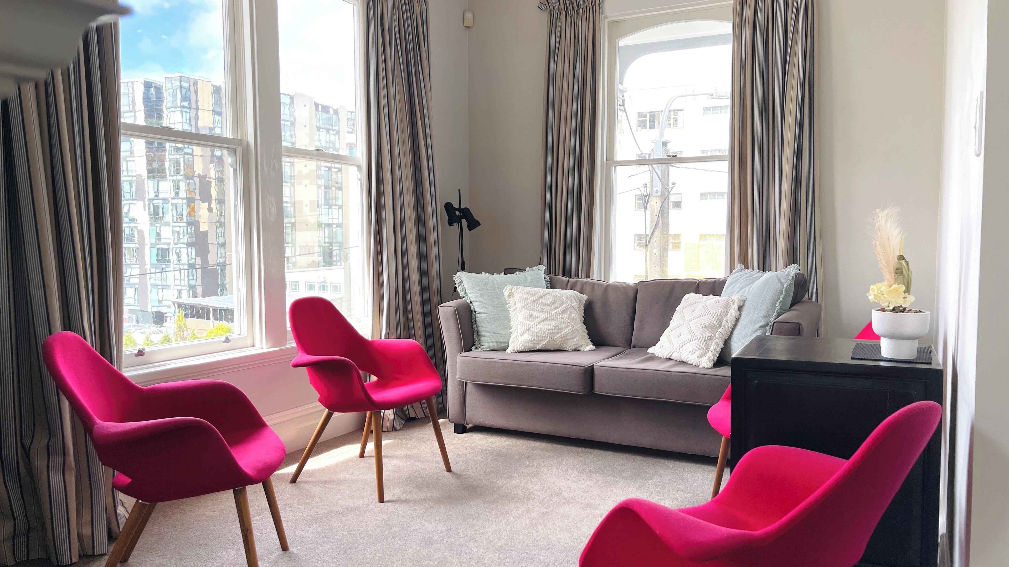A modern living room with a grey sofa, two red chairs, and a small table with a plant.