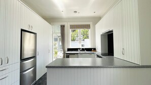 Una cocina moderna con armarios blancos, un refrigerador de acero inoxidable, horno empotrado y un ventanal con cortinas.