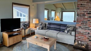 A living room with a TV, fan, and coffee table. - NEW LISTING! Fantasea! Enjoy dramatic crashing waves, fireplace, dog friendly! (Yachats)