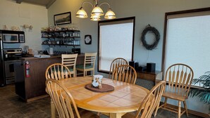 A dining area with a wooden table and chairs, a kitchen in the background, and a large window with a view. - NEW LISTING! Fantasea! Enjoy dramatic crashing waves, fireplace, dog friendly! (Yachats)