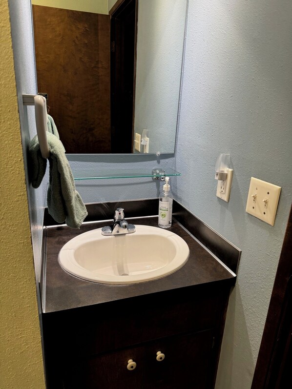 Une salle de bain avec un lavabo blanc, une étagère en verre, un miroir et un porte-serviettes.
