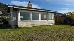 A single-story building with large windows and a chimney, surrounded by a grassy yard. - NEW LISTING! Fantasea! Enjoy dramatic crashing waves, fireplace, dog friendly! (Yachats)